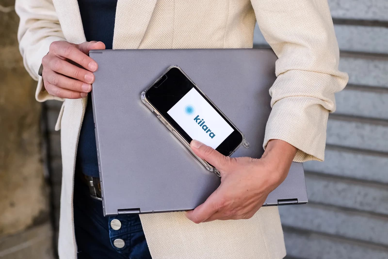 Leila Steiner hält einen Laptop und ein Smartphone, auf dem Display das kilara-Logo.